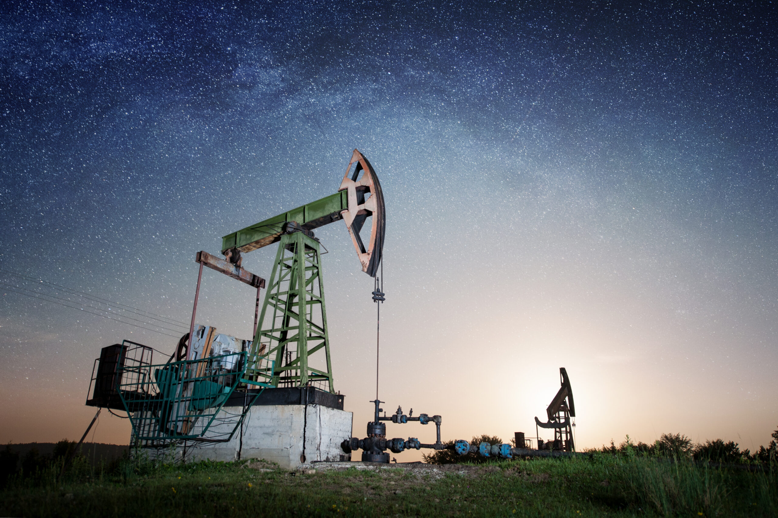 Oil pumps are working on the oil field in the evening under night sky with stars. Milky way. Oil industry equipment