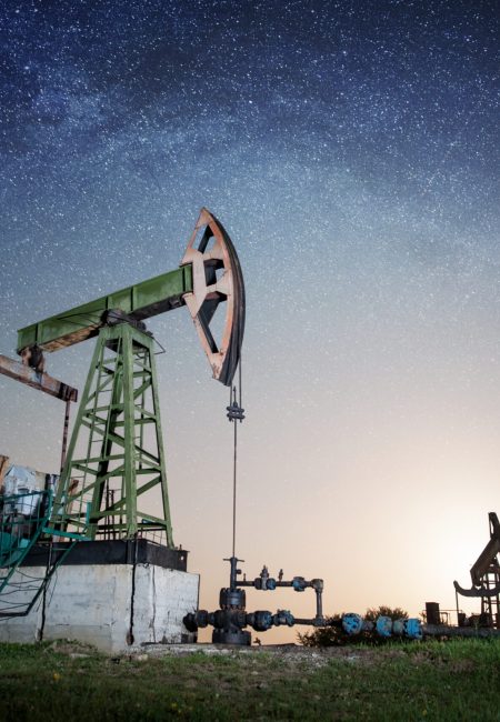 Oil pumps are working on the oil field in the evening under night sky with stars. Milky way. Oil industry equipment